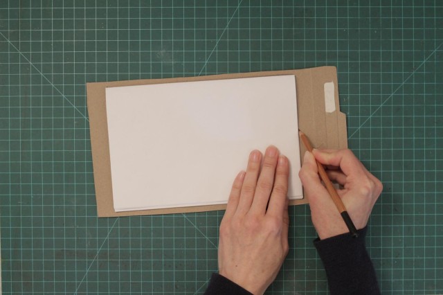 Placing paper on one of the cardboard pieces and tracing the contour of the pages