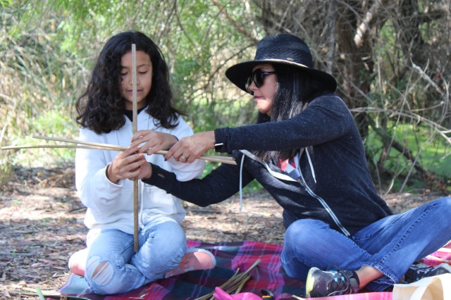 two people weave a plant 