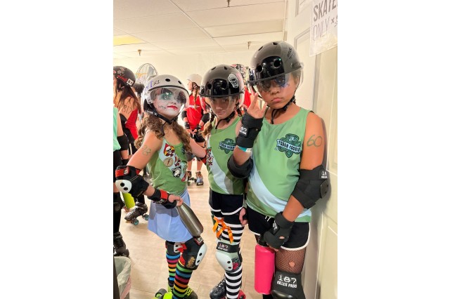 Three young girls in green roller derby uniforms posing as &quot;tough cookies&quot;