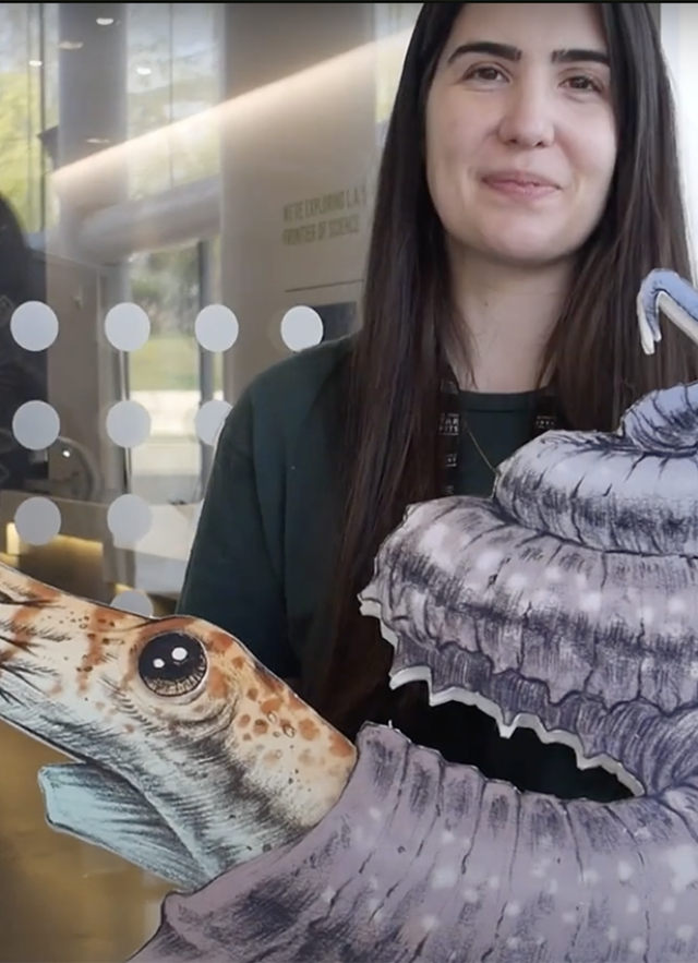 Juliet Hook holding a flat cut-out of an ammonite with a purple shell and orange and white striped head with tentacles 