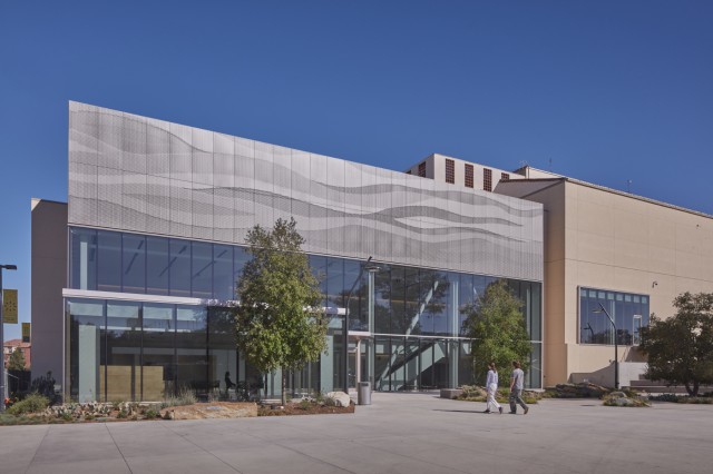 Two people walking into a silver building with a wall windows