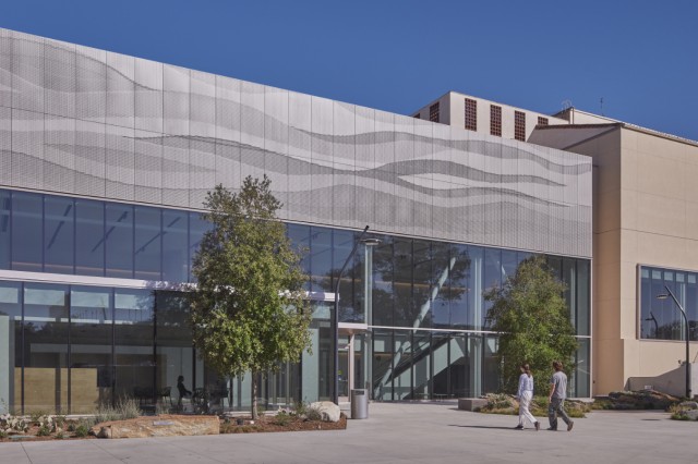 Two people walking towards a silver building with a wall of windows