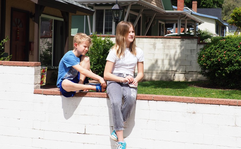 two kids, a boy and girl, sit on a low wall 