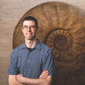 Head and shoulders portrait of Austin Hendy with fossil in the background